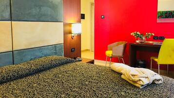 Habitación de hotel con una cama, un escritorio y una silla. La pared es roja y el cabecero de madera.