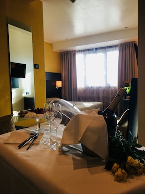 A hotel room with a neatly arranged dining table, a bed, a window with curtains, and a television on the wall.