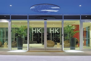 A modern building facade with large glass doors, potted plants, and the letters "HK" prominently displayed.
