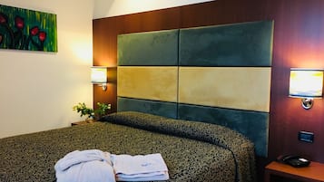 Une chambre d’hôtel avec un grand lit, une tête de lit ornée d’un motif géométrique, une table de chevet avec une lampe et un tableau accroché au mur.
