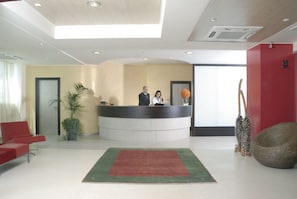 A reception area with a reception desk, a red chair, a green rug, and a potted plant.