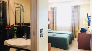 Quarto de hotel com banheiro, duas camas, uma escrivaninha e um laptop.