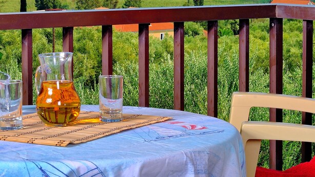 A table with a pitcher and glasses, overlooking a coastal landscape with houses and mountains. - Kleopatra Studios (Zakynthos)