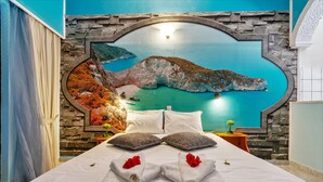 A hotel room with a large bed, a stone wall, and a mural of a coastal landscape. - Kleopatra Studios (Zakynthos)