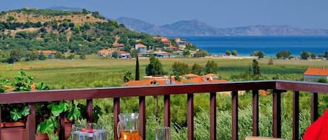 A table with a pitcher and glasses on a balcony overlooking a coastal landscape with houses and hills.