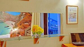 A hotel reception desk with a glass partition, a laptop, and framed pictures on the wall. - Kleopatra Studios (Zakynthos)