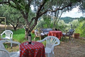 An outdoor seating area with white plastic chairs and tables, a bottle of wine, and a view of a lush landscape. - Kleopatra Studios (Zakynthos)
