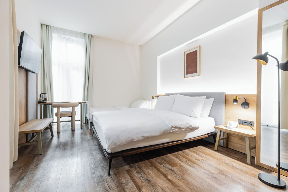 A hotel room with a bed, a desk, a chair, a TV, and a lamp.