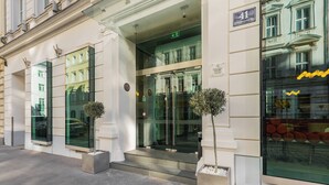 Un edificio moderno con entrada de vidrio, un letrero que indica la dirección y el reflejo de otro edificio en el vidrio.