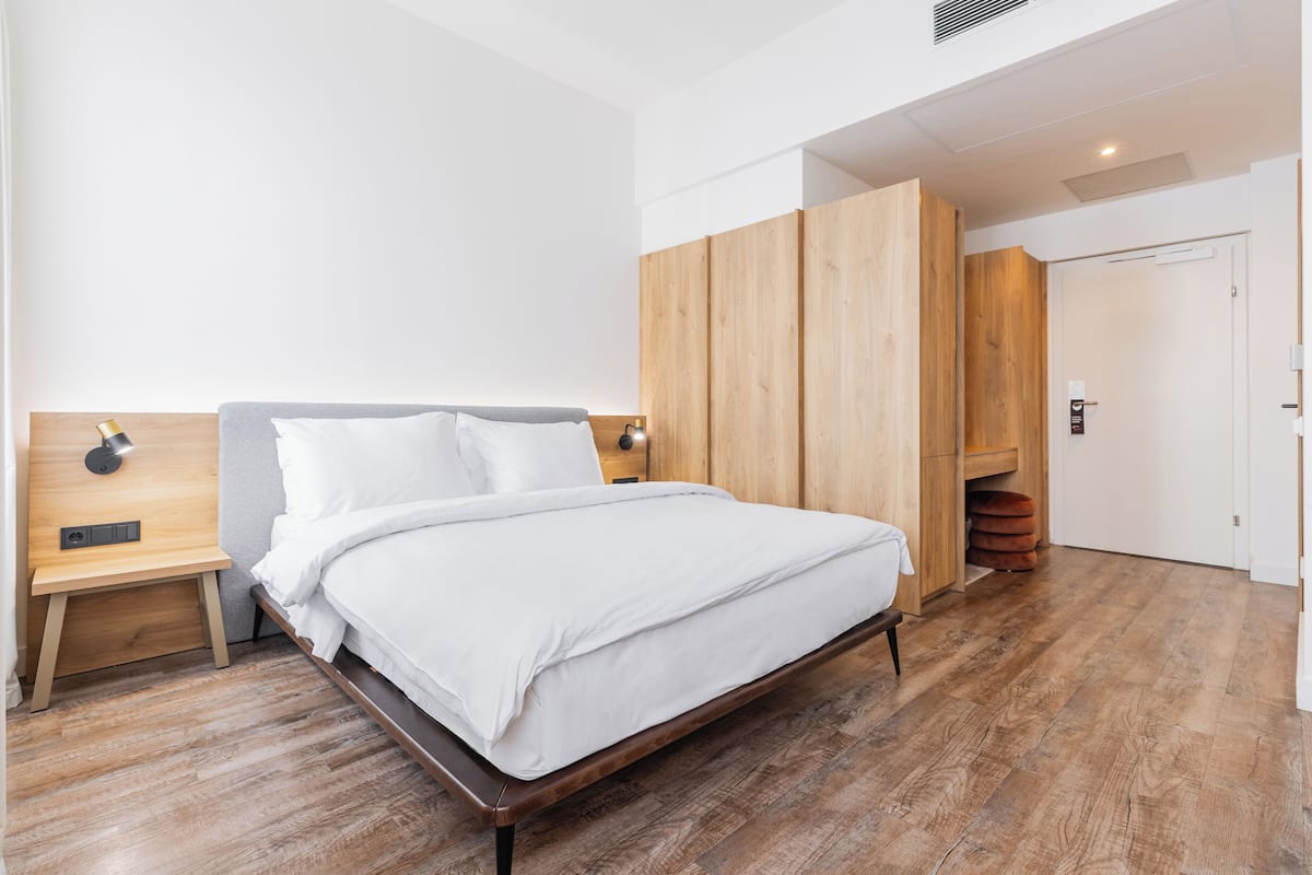 A modern hotel room with a wooden bed frame, a nightstand, and a wardrobe.