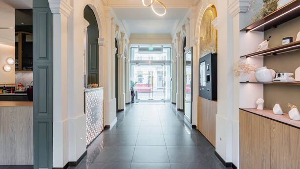 Un pasillo de hotel de diseño moderno, con un camino central, iluminación decorativa y una zona de recepción con mostrador y elementos decorativos.