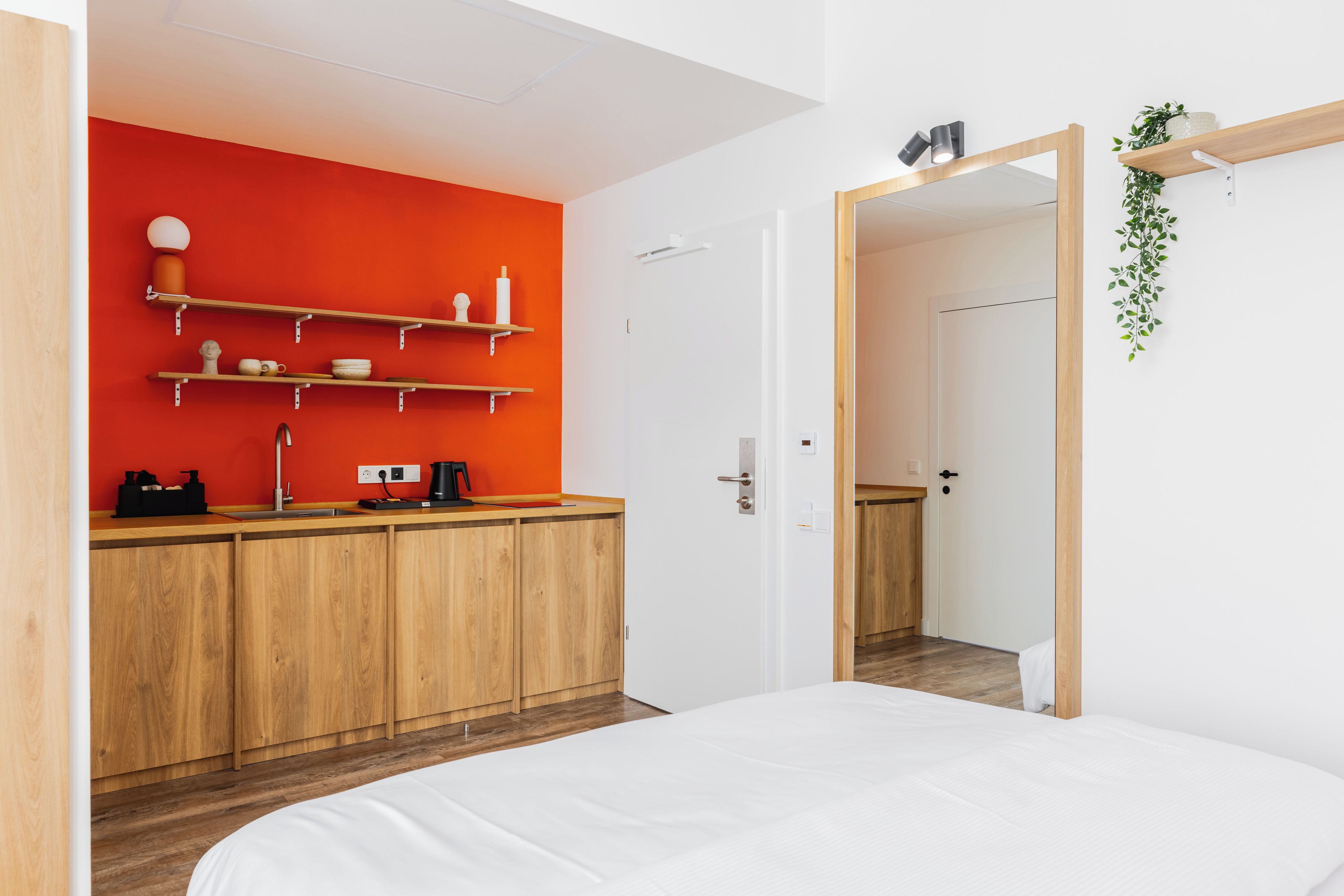 Une chambre moderne avec un lit, une armoire en bois, un mur d’accent rouge et un miroir.