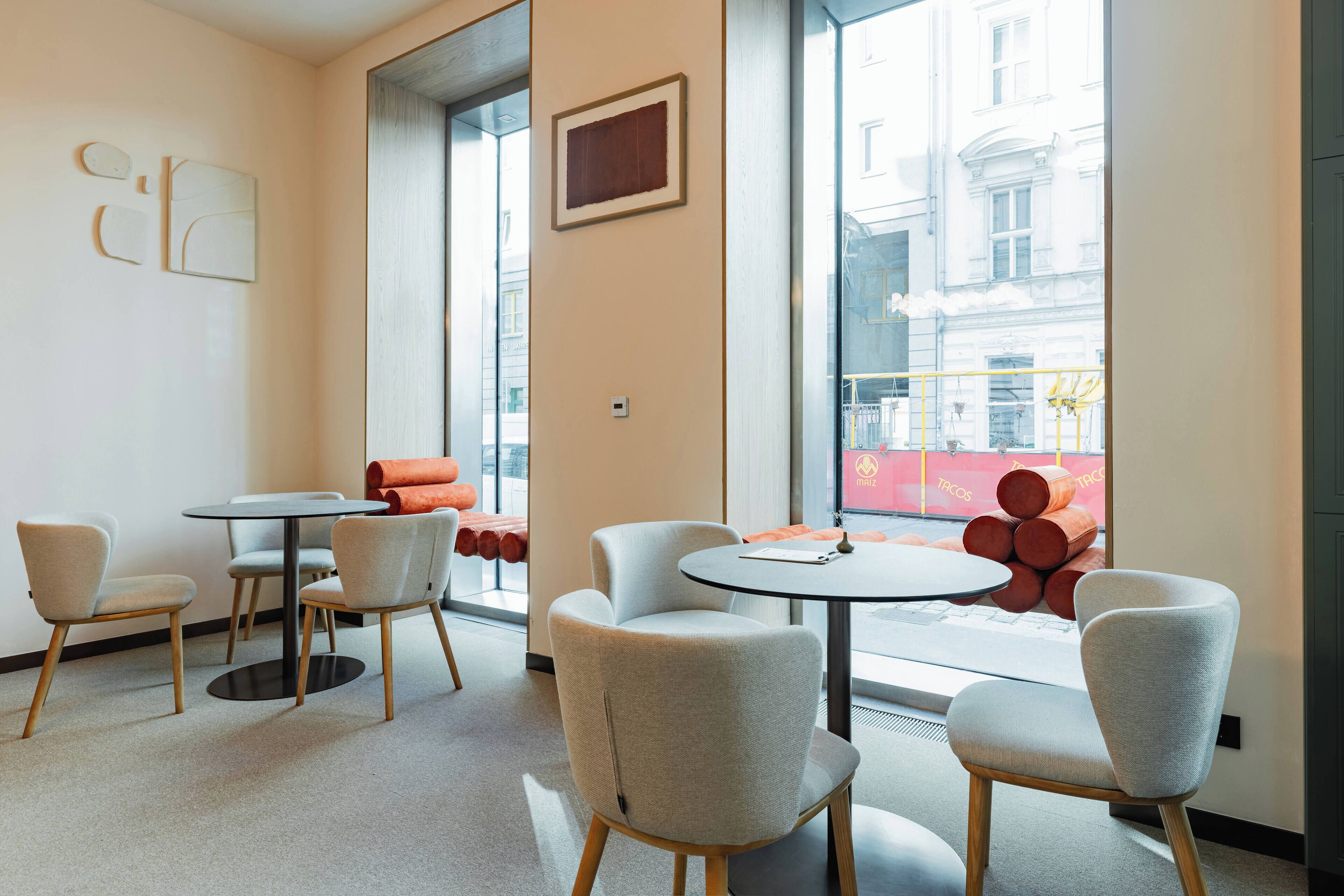 A modern interior with round tables and chairs, large windows, and a view of the street.