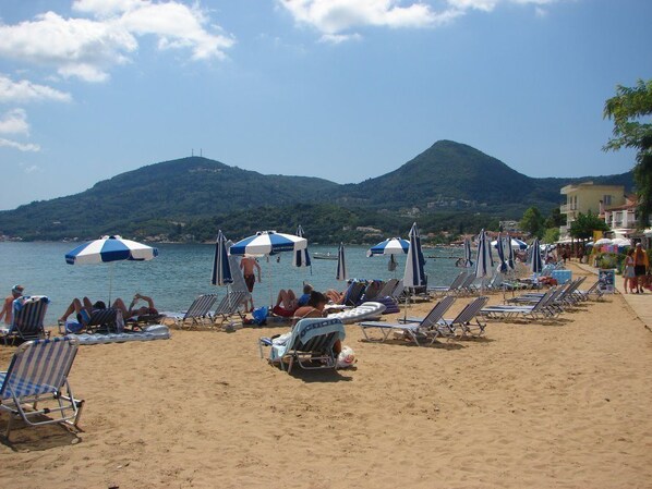 A beach with rows of sun loungers and umbrellas, a clear sky, and a mountain in the background.