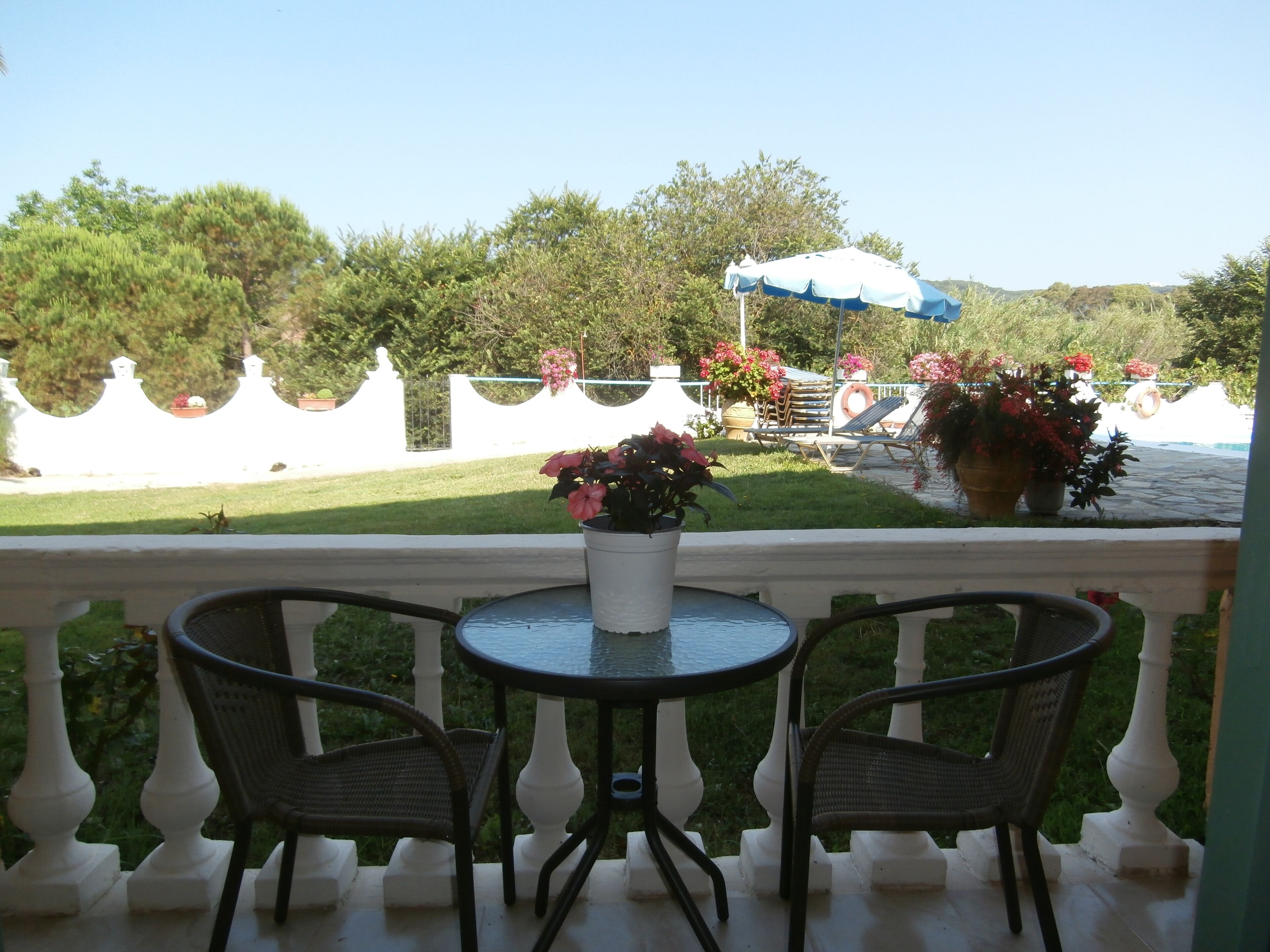Ein Balkon mit Tisch und Stühlen, einem Blumentopf und einem Poolbereich mit Liegestühlen und Sonnenschirmen.