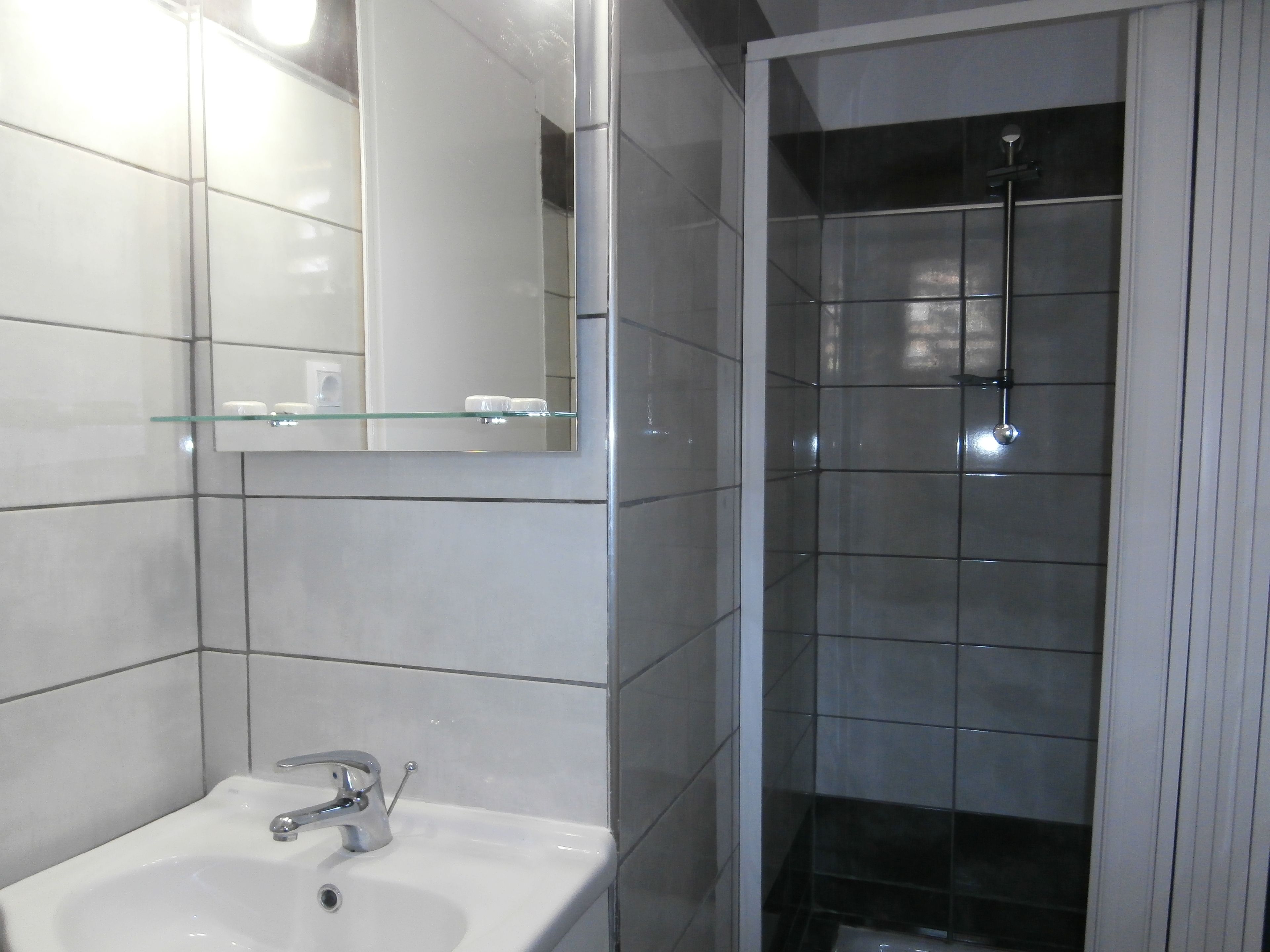 A bathroom with a white sink, a glass shelf, and a shower area.