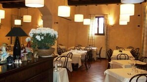 A restaurant interior with multiple tables and chairs, warm lighting, and a central decorative plant. - Albergo Ca' Vecchia (Sasso Marconi)