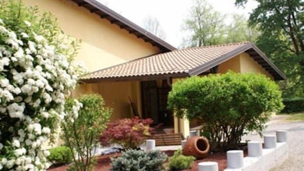 A house with a tiled roof, a porch, and a garden with various plants and a white flower bush. - Albergo Ca' Vecchia (Sasso Marconi)
