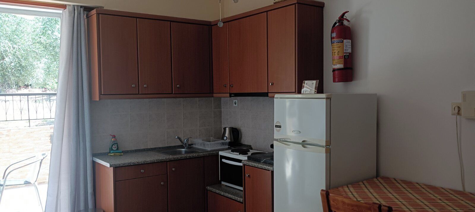 Una cocina compacta con armarios de madera, un refrigerador blanco y un extintor de incendios en la pared.