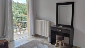 A bedroom with a large bed, a dresser with a mirror, a radiator, and a view of a balcony with a table and chairs. - Katerina Apartments (Kalamata)