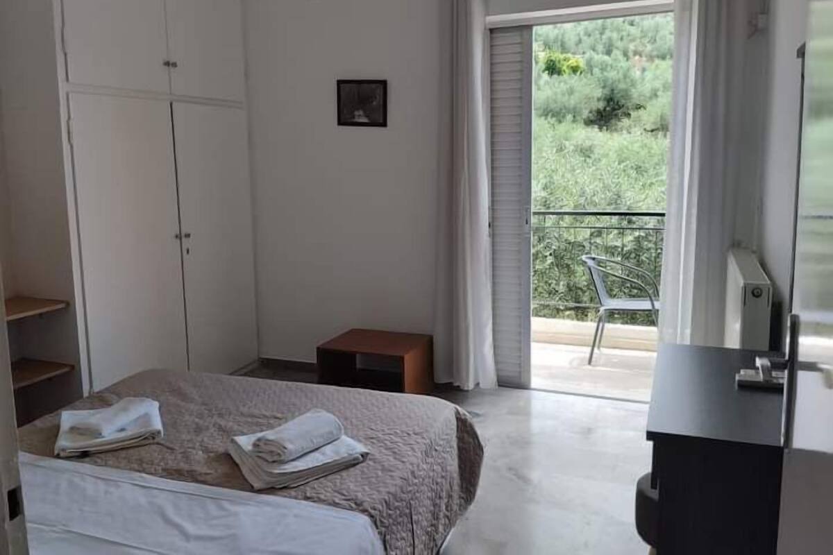 A bedroom with a bed, a small table, a wardrobe, and a balcony with a chair.