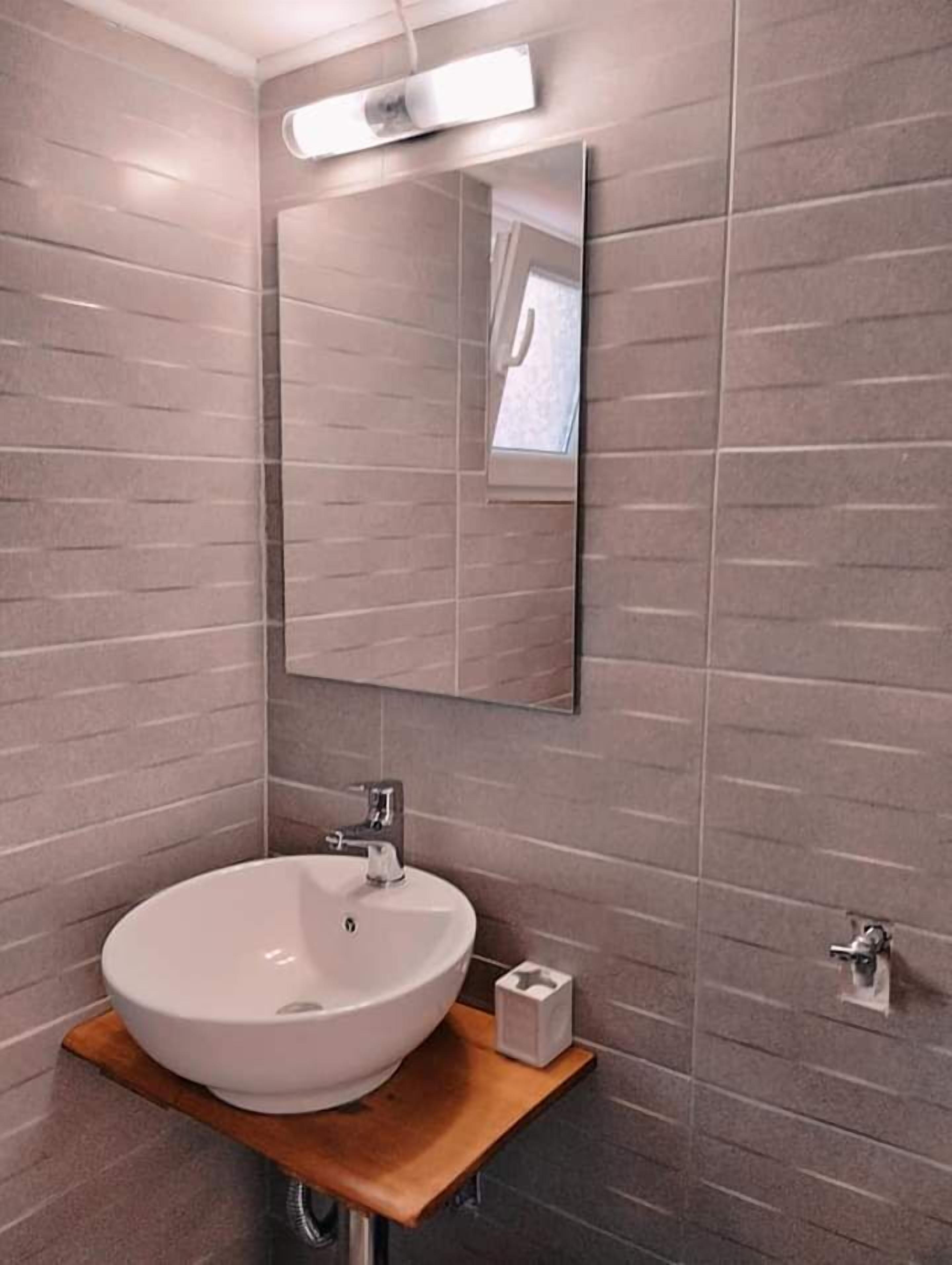 Une salle de bain moderne avec un grand lavabo sur pied, un miroir et un petit distributeur de savon placé sur une étagère en bois.