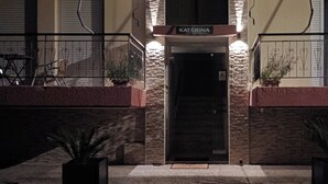 A hotel entrance with a sign reading "KATERINA," a stone facade, and potted plants on either side. - Katerina Apartments (Kalamata)
