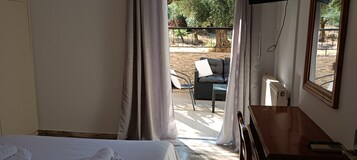 Quarto de hotel com uma cama, uma escrivaninha de madeira e vista para uma área de estar externa.