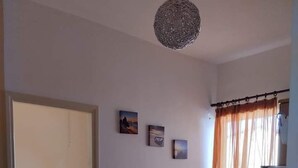A room with a bed, a dining table with chairs, and a small seating area. There are three paintings on the wall. - Katerina Apartments (Kalamata)