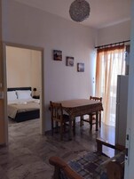 A room with a bed, a dining table with chairs, and a small seating area. There are three paintings on the wall.