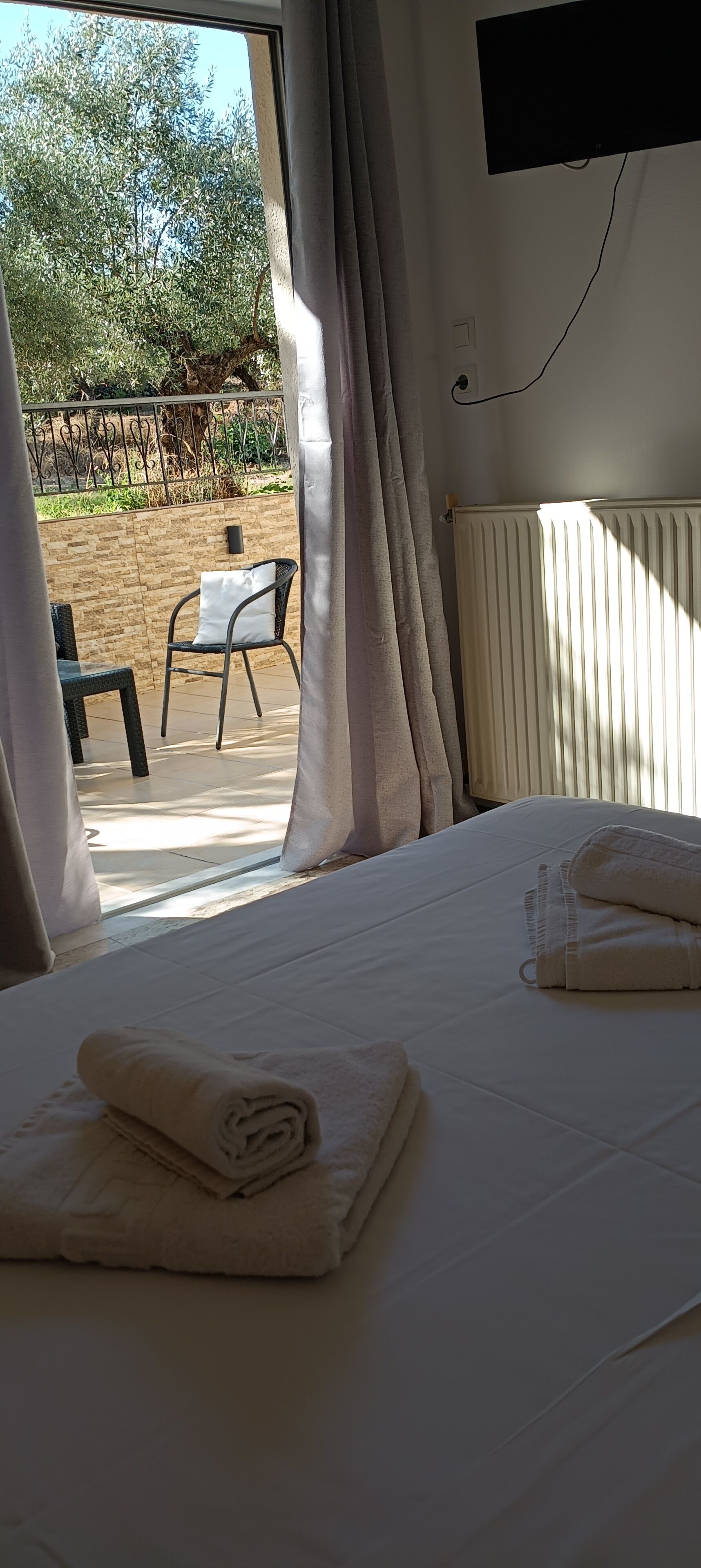 A hotel room with a bed, a window with curtains, a view of the outdoors, and a table with chairs outside.