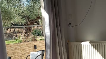 A hotel room with a bed, a window with curtains, a view of the outdoors, and a table with chairs outside.