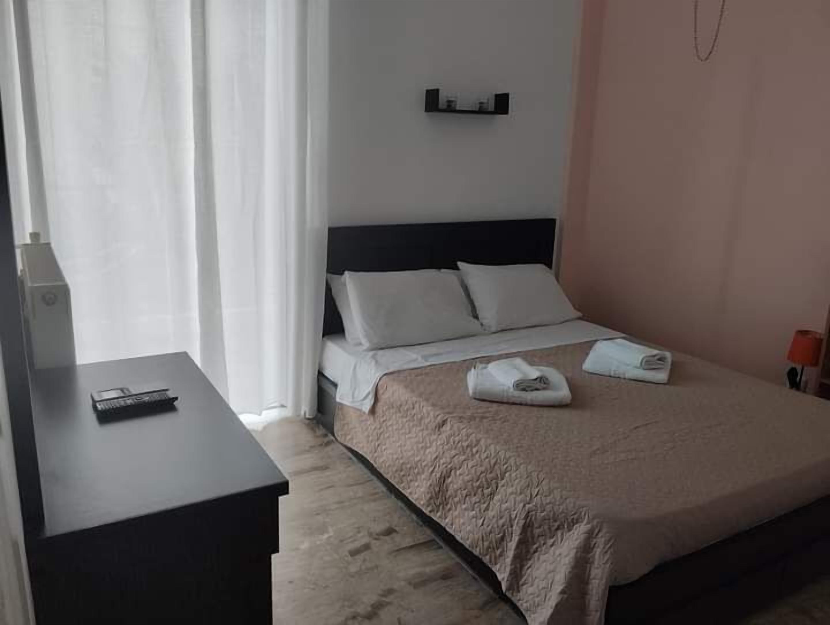 A hotel room with a bed, a bedside table, a TV, and a window with curtains.