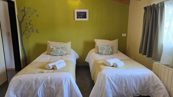 Habitación de hotel con dos camas individuales, cada una con una almohada y una toalla enrollada.