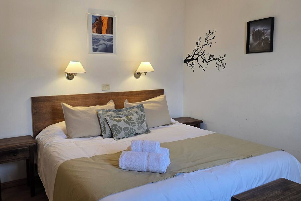 A neatly made bed with a wooden headboard, two wall-mounted lamps, and a framed picture above it.