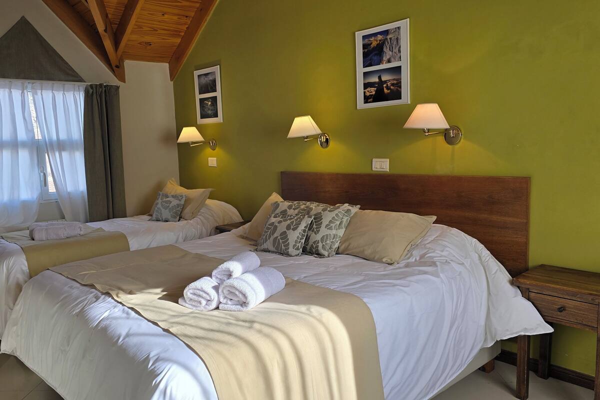 A hotel room with two beds, a wooden headboard, and wall-mounted lamps.