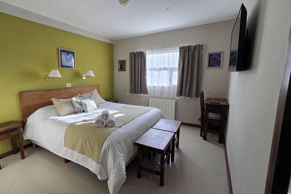 A hotel room with a bed, bedside tables, a desk, and a television.