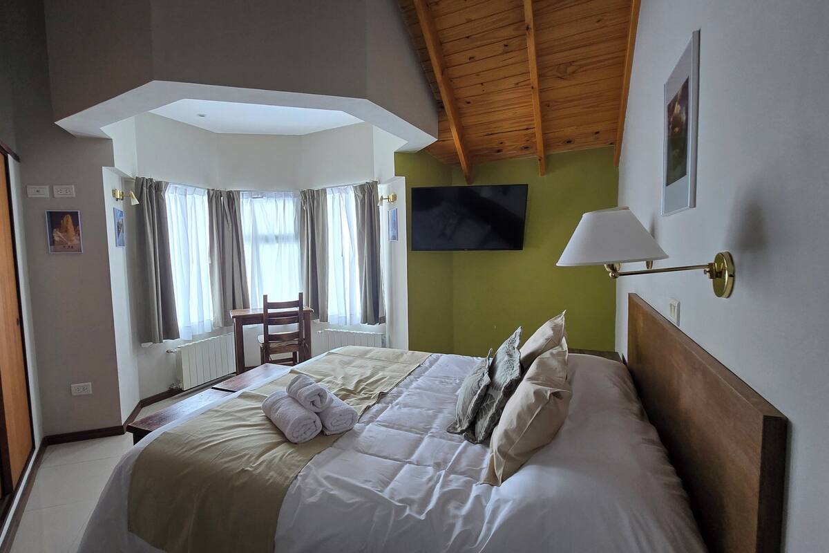 A hotel room with a large bed, a desk, a chair, a TV, and a window with curtains.