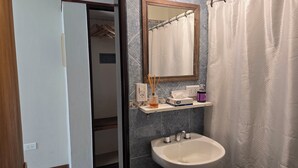 A bathroom with a white sink, a mirror, a shelf with toiletries, and a shower curtain. - Cumbres Nevadas - Hostería Boutique (El Chalten)