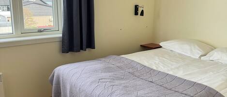 Une chambre à coucher avec un lit, une fenêtre avec des rideaux, un luminaire fixé au mur et un tableau.