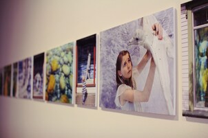 Una serie de obras de arte enmarcadas en una pared, incluyendo una pintura de una persona sosteniendo un ave blanca.