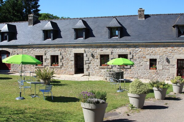 A stone building with a sloped roof, outdoor seating with green umbrellas, and potted plants. - Domaine de Lesvaniel (Landudec)