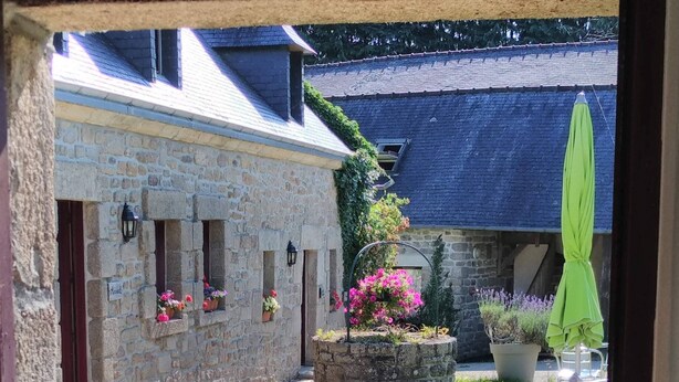 Un edificio de piedra con una ventana, un jardín lleno de flores y una mesa con sillas afuera.