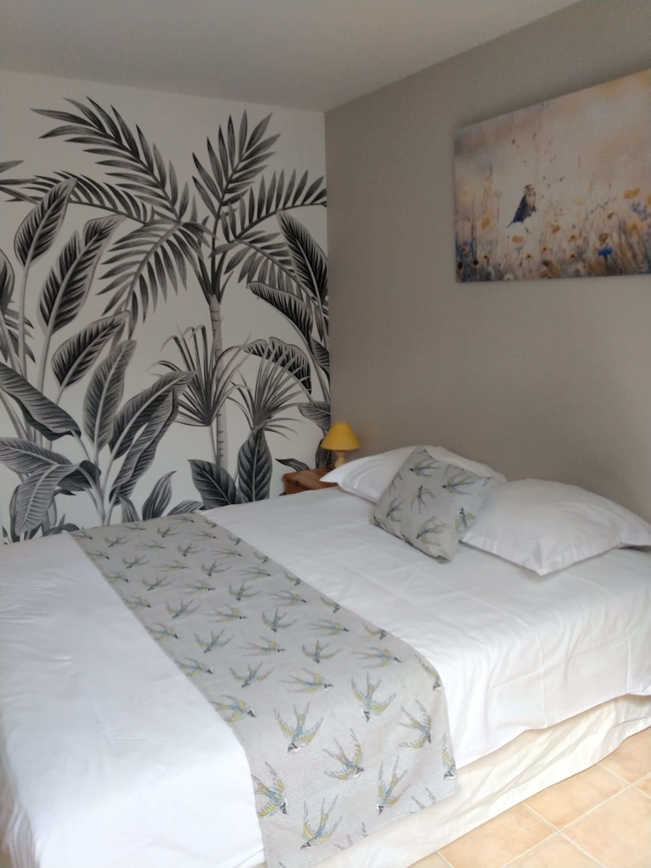 A bedroom with a bed, a nightstand, a lamp, and a wall with a tropical leaf pattern.