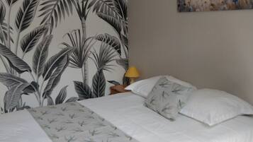 A bedroom with a bed, a nightstand, a lamp, and a wall with a tropical leaf pattern.