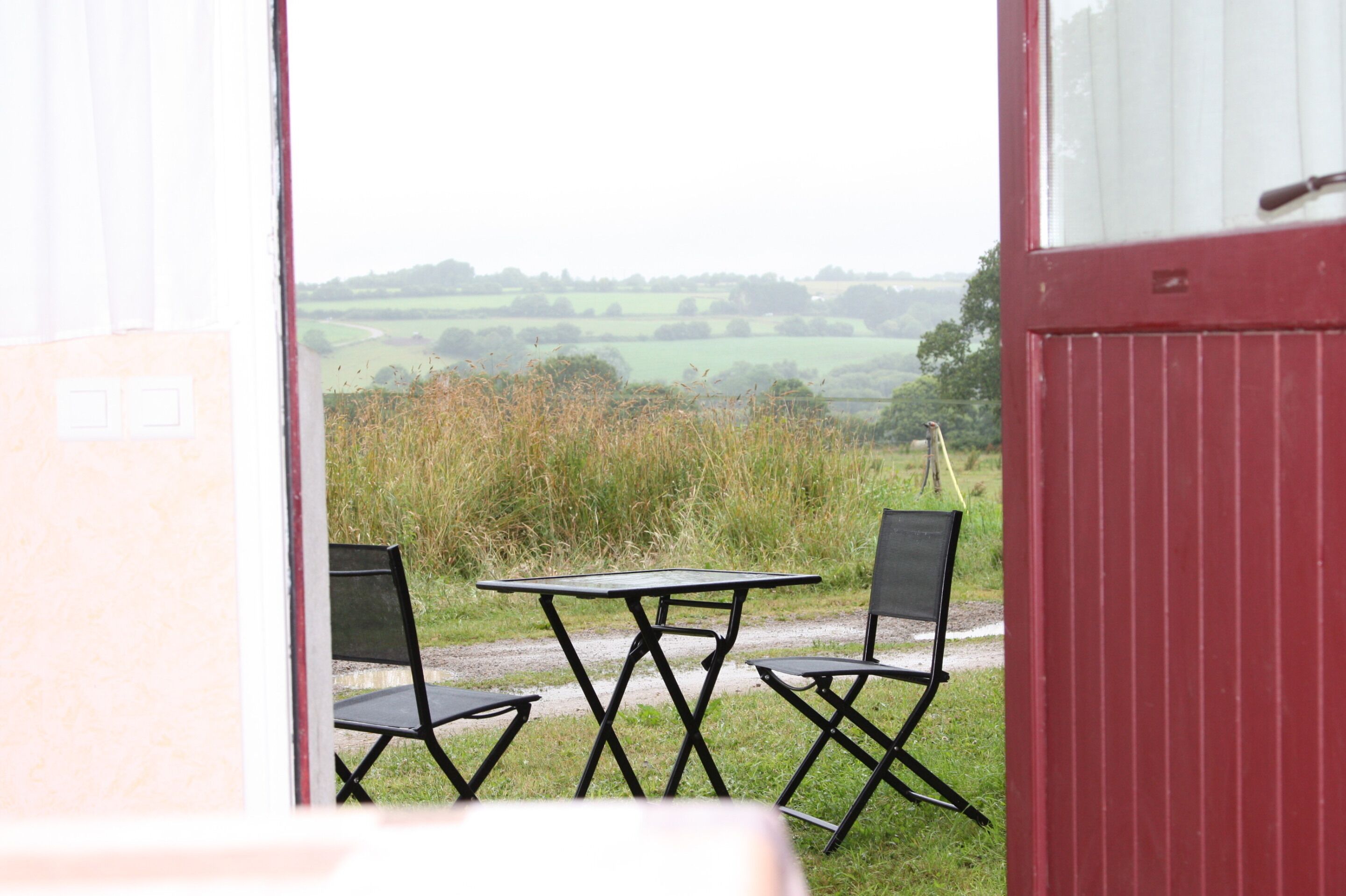 A view from a room with a table and two chairs, looking out to a rural landscape.
