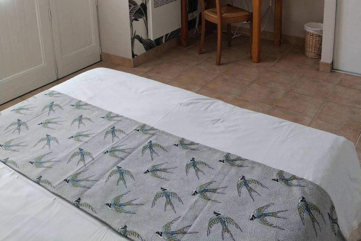 A hotel room with a bed, a desk, a chair, a television, and a wall with a leaf pattern.