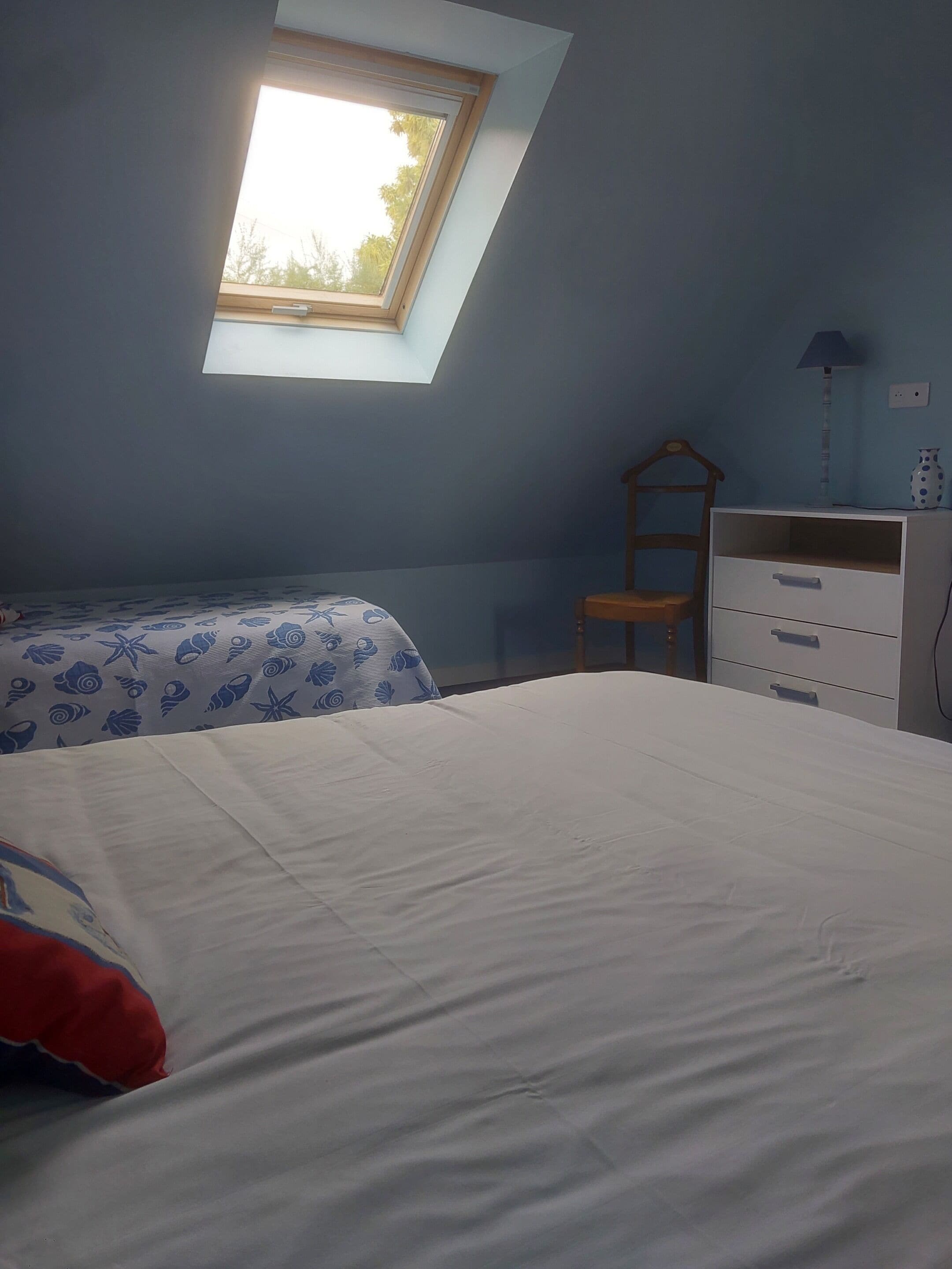 Un dormitorio con tragaluz, cama, una silla y cómoda.