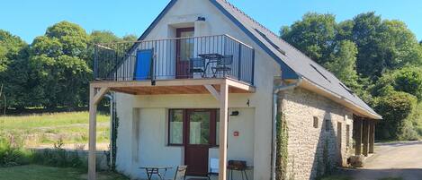 A two-story stone house with a balcony, a front door, and a small porch area with outdoor furniture.