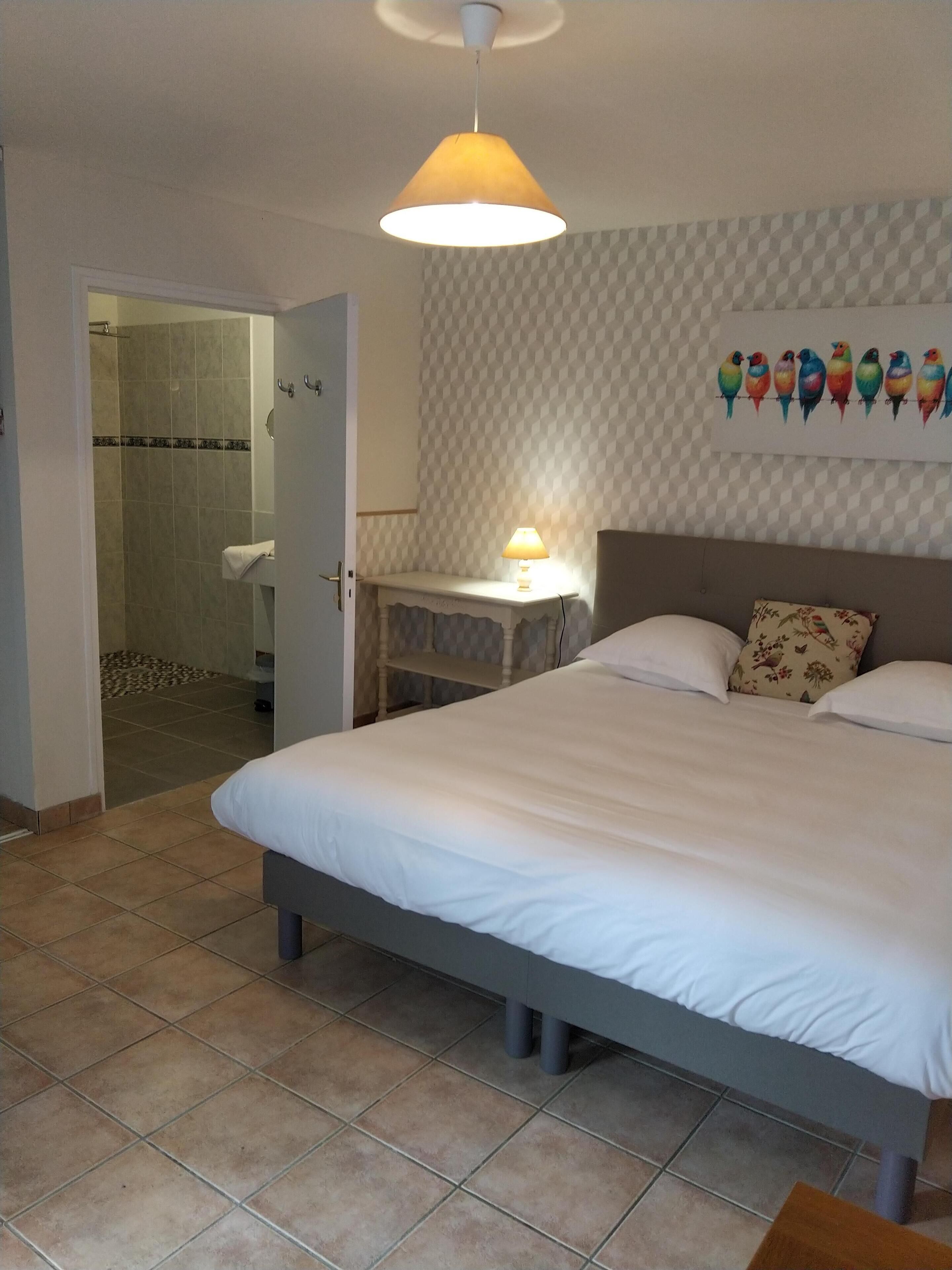 Un dormitorio con cama, mesita de noche, lámpara, pared con un mural de aves y zona de ducha.